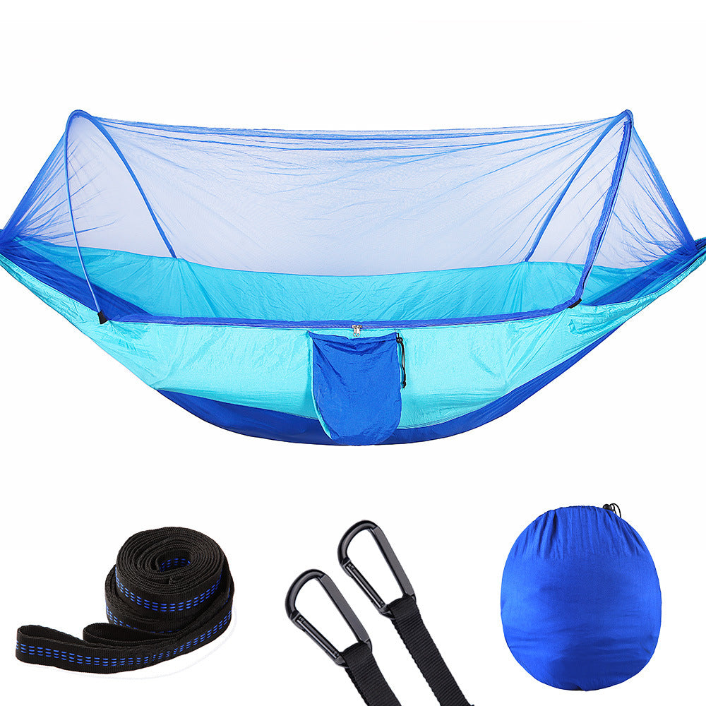 Two people sitting in a blue hammock with mosquito net in a forest setting