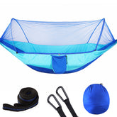 Two people sitting in a blue hammock with mosquito net in a forest setting