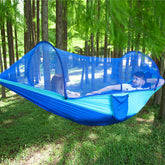 Two people sitting in a blue hammock with mosquito net in a forest setting