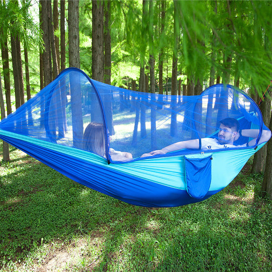 Two people sitting in a blue hammock with mosquito net in a forest setting