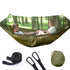 Two people sitting in a blue hammock with mosquito net in a forest setting